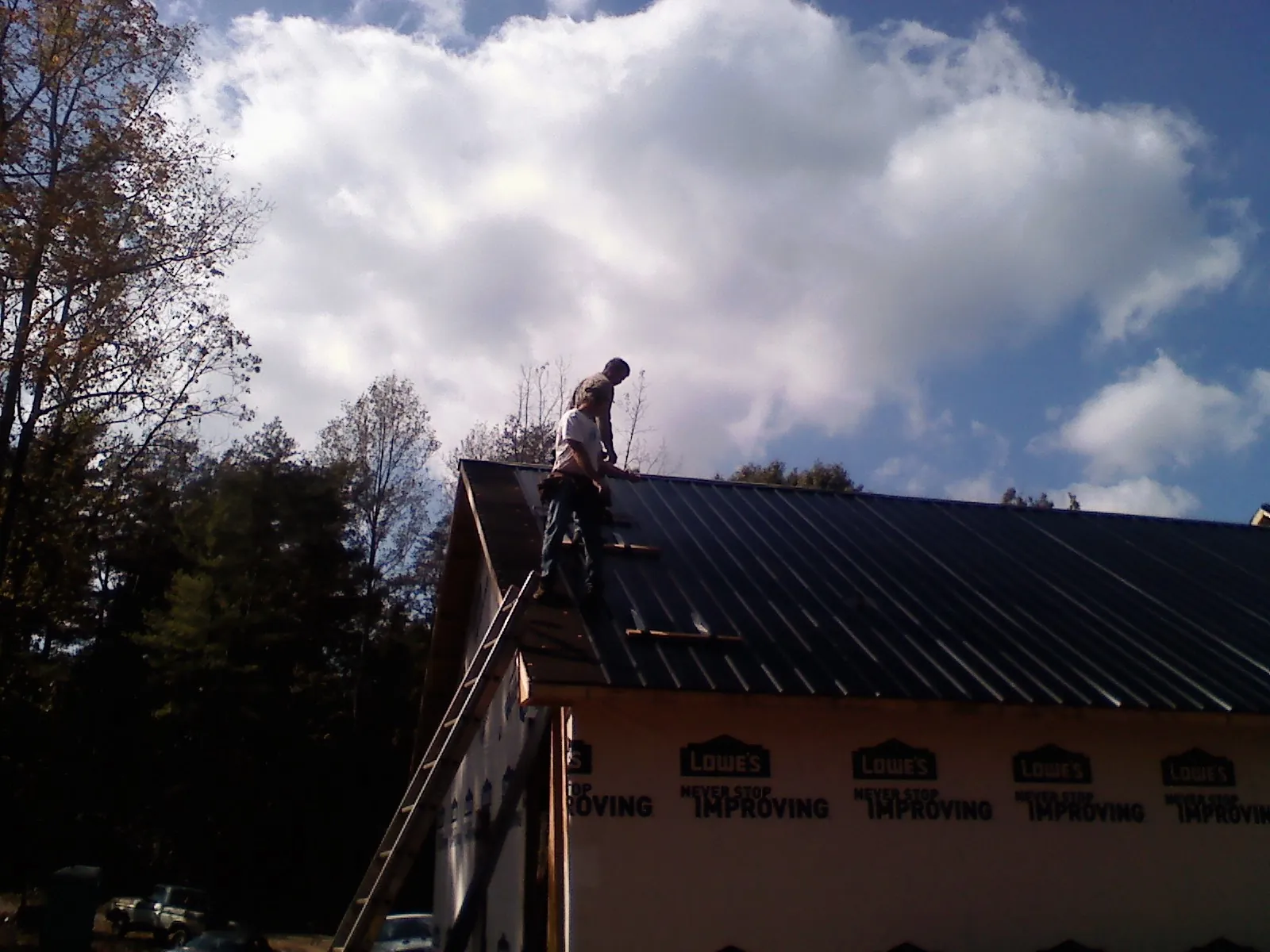 Roofer fastening dark metal panels high against a cloudy sky, from a Roof Inspection job in Sunset